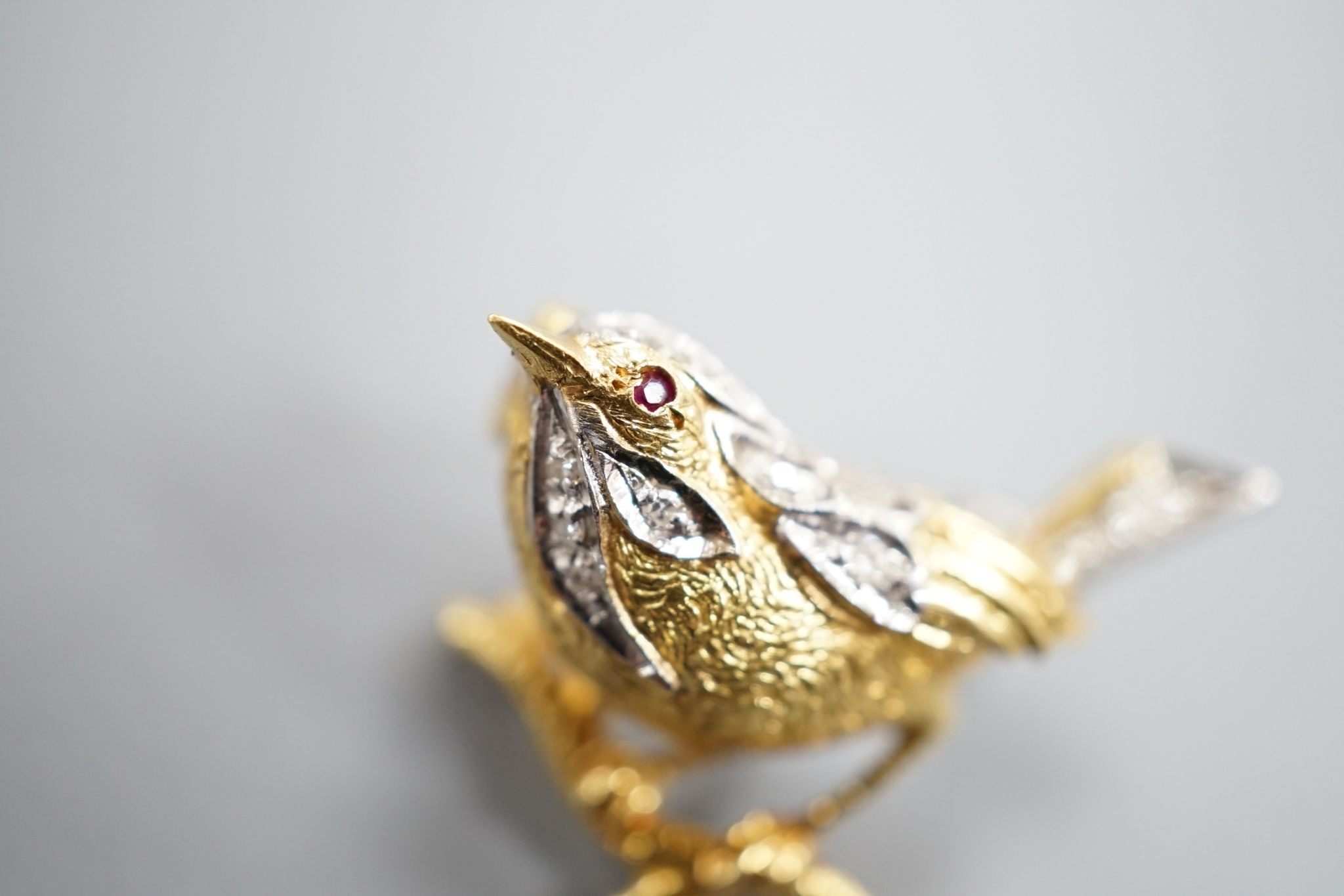 A modern textured 18ct two colour gold, ruby and diamond set bird brooch, 24mm, gross weight 6 grams.